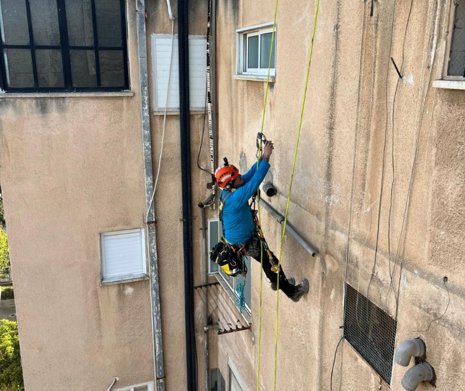 סאם תלוי על חבלי סנפלינג ועובד על קיר חיצוני של בניין